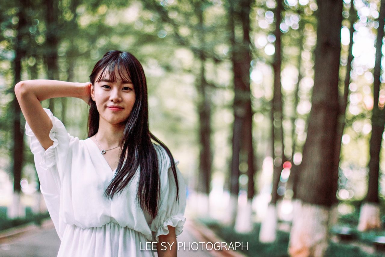 young adult, person, focus on foreground, lifestyles, young women, long hair, portrait, looking at camera, leisure activity, casual clothing, smiling, front view, waist up, tree, standing, happiness, headshot