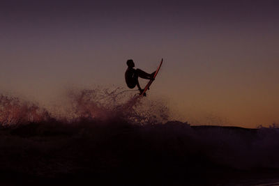 Silhouette man in mid-air against sky during sunset