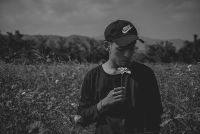 Man holding flower while standing on land against sky