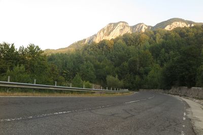 Road by trees and mountains against sky