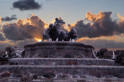 Statue by fountain against sky during sunset