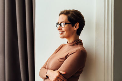 Side view of smiling woman standing by wall at home