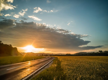 Road amidst field against sky during sunset