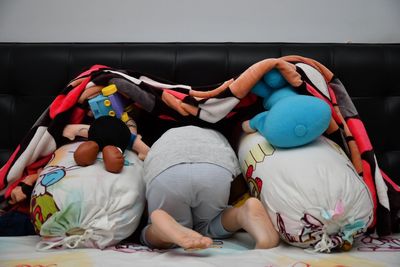 Child hiding with toys below blanket on bed at home