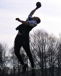 Low angle view of man jumping on bare tree