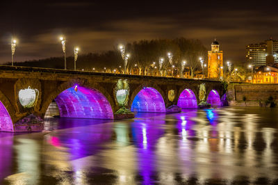 Illuminated bridge over river in city at night