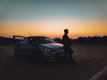 Silhouette man standing by car against sky during sunset