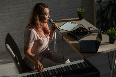 Young woman playing piano against wall at home