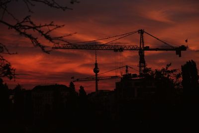 Silhouette cranes and buildings against sky during sunset