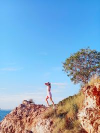 Rear view of woman standing on rock against clear blue sky