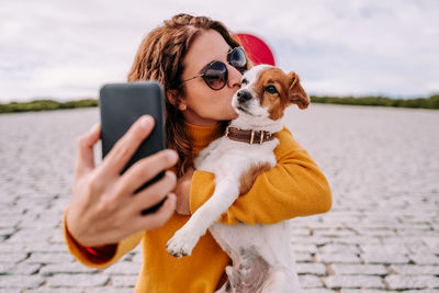 Smiling woman taking selfie while standing with dog outdoors