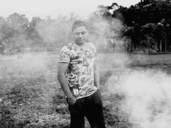 Thoughtful man standing by smoke on field against trees