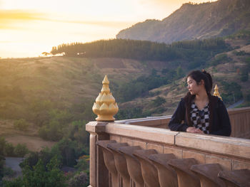 Woman sitting on mountain against sky