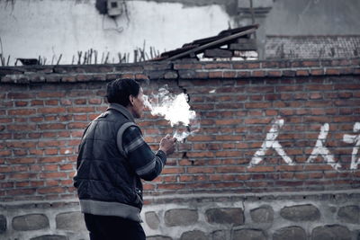 Man smoking cigarette while standing by brick wall