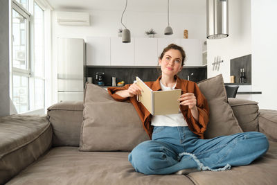 Young woman using phone while sitting on sofa at home