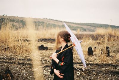 Woman with umbrella standing on field against sky