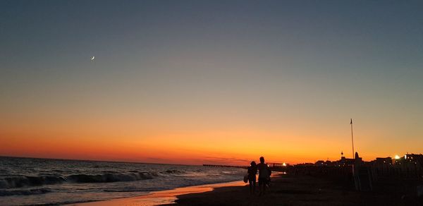 Silhouette people on beach against clear sky during sunset