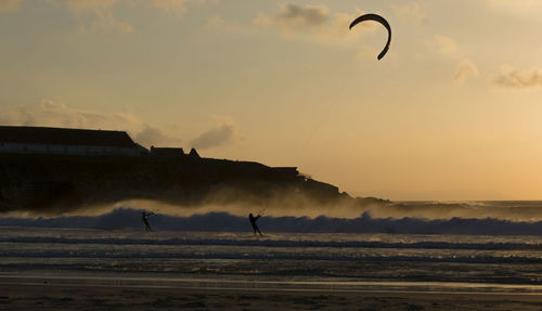 Silhouette people kiteboarding on sea against sky during sunset