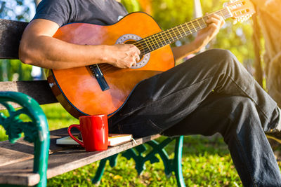 Midsection of man playing guitar while sitting on bench
