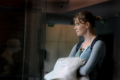 Thoughtful woman holding jacket while standing in room