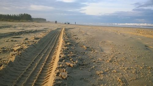 Tire tracks on sand dunes at beach against sky