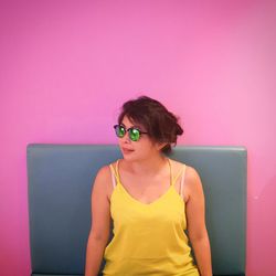 Young woman wearing sunglasses standing against wall