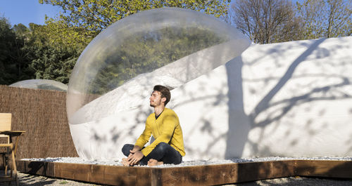 Young man enjoying sunlight in front of transparent dome hotel