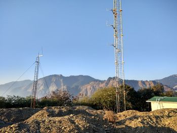 Electricity pylons by mountains against clear blue sky