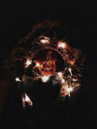 Woman wearing fur coat with illuminated string lights against black background