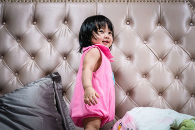 Little girl with bob hairstyle wearing a pink dress standing on the bed. happy people concept.