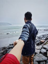 Rear view of friends at beach against sky