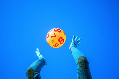 Low angle view of person catching yellow ball against blue background