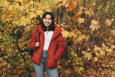 Portrait of smiling young woman standing by autumn leaves