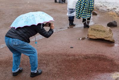 Man with umbrella photographing stone