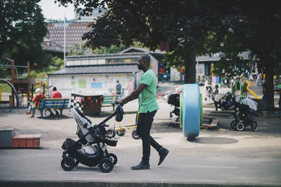 Man pushing baby stroller while walking on road at park