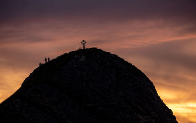 Silhouette cross on mountain against sky during sunset