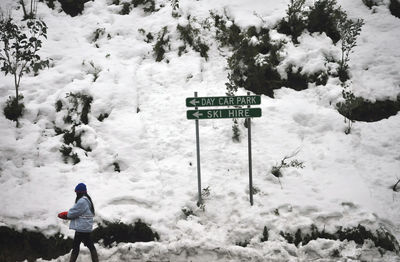 Side view of woman walking by sign board on snowcapped mountain