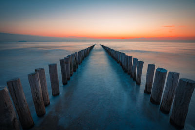 Wooden posts in sea against sky during sunset