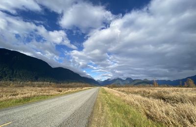 Empty road amidst field against sky