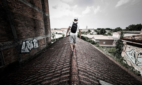 Rear view of man walking on roof in city against sky