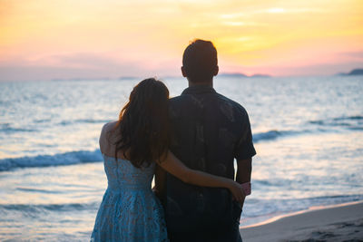 Rear view of couple standing at beach during sunset