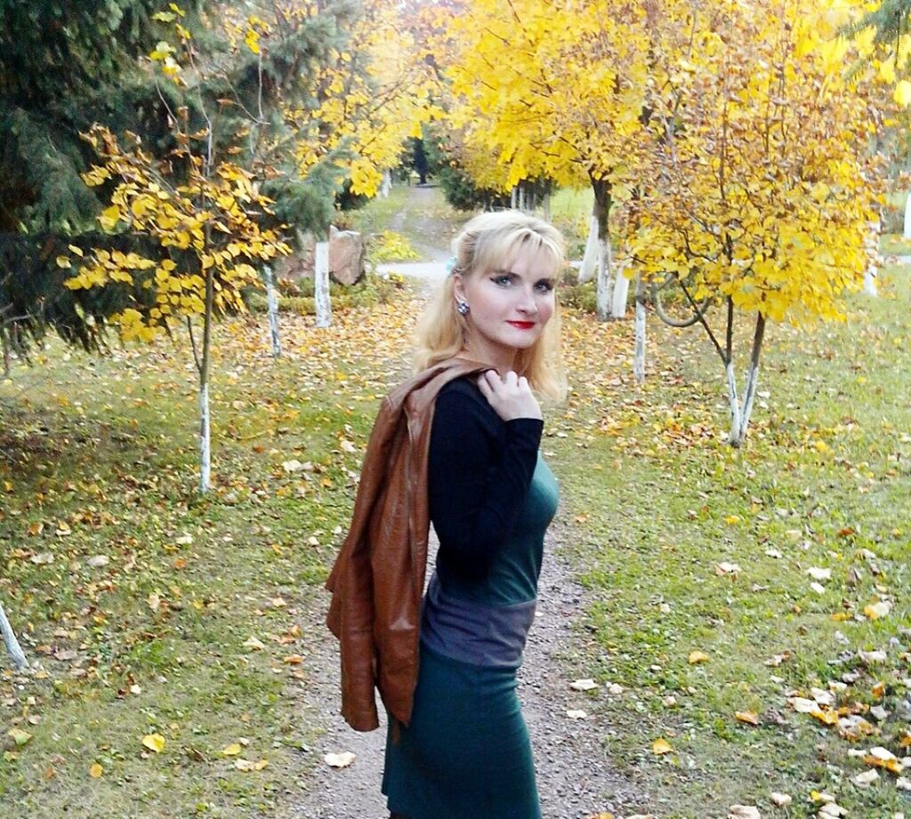 BEAUTIFUL YOUNG WOMAN STANDING BY LEAVES IN PARK