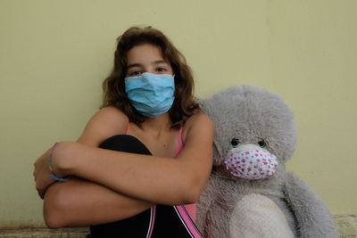 Portrait of cute girl sitting with toy against wall