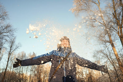 Low angle view of man throwing snow mid air during winter