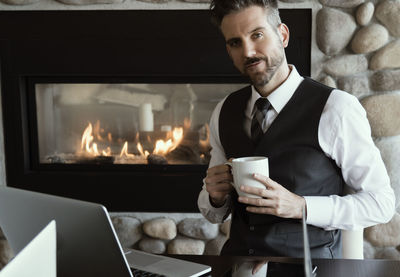 Portrait of businessman having coffee while using laptop at home