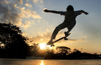 Silhouette man with skateboard jumping against sky during sunset