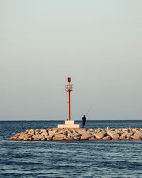 Lighthouse by sea against clear sky