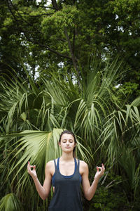 Teenager meditating in lotus position against plants