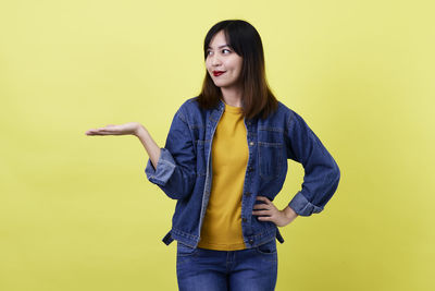 Portrait of young woman standing against yellow background