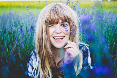 Smiling young woman holding lavender flowers over eye while sitting in field